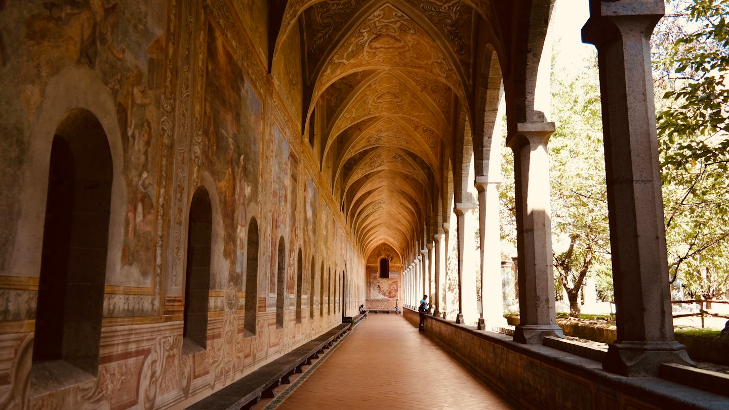La luce del sole filtra attraverso le colonne ad arco in pietra di un chiostro storico.