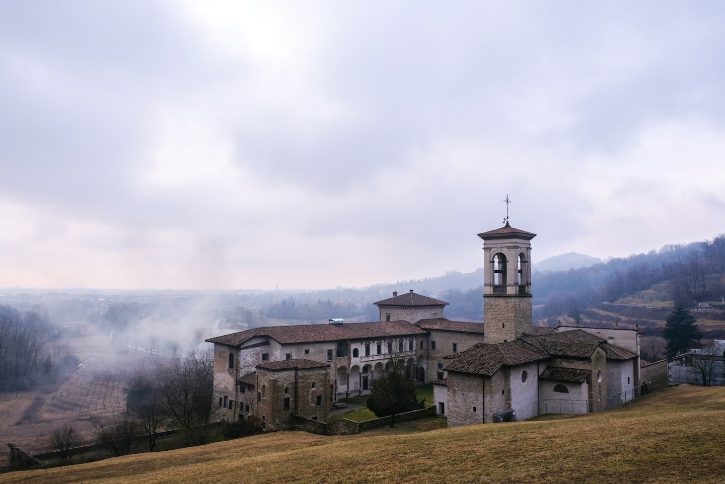 Monastero in pietra storico con campanile su un pendio erboso.