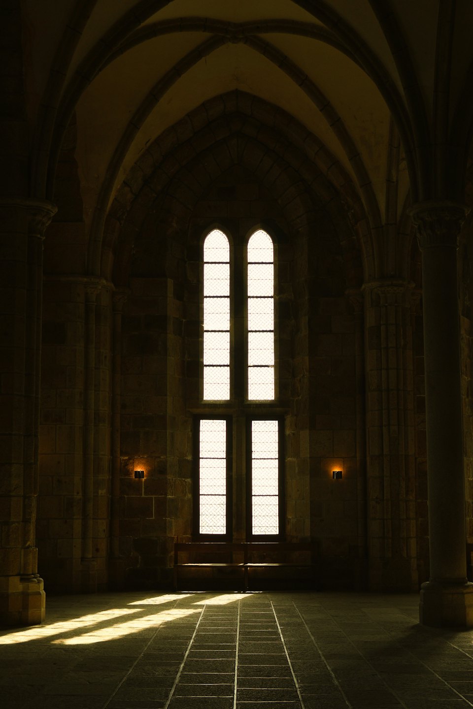 La luce del sole filtra attraverso finestre ad arco in un salone storico di pietra.