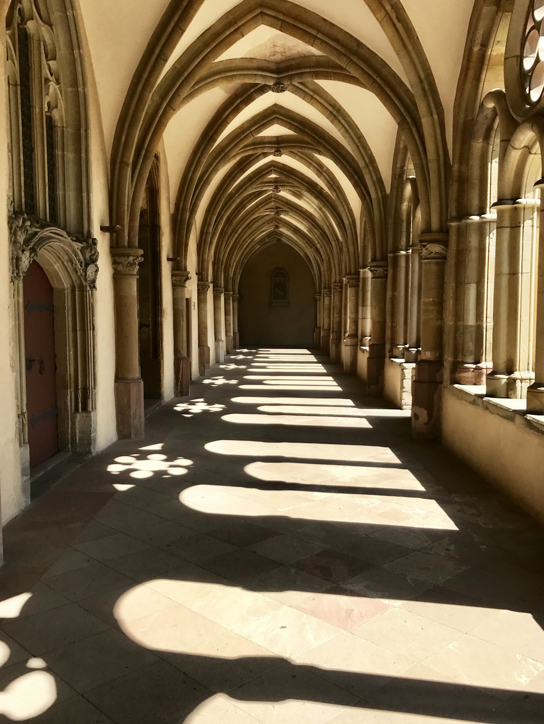 La luce del sole filtra attraverso un corridoio vuoto di un chiostro in pietra.