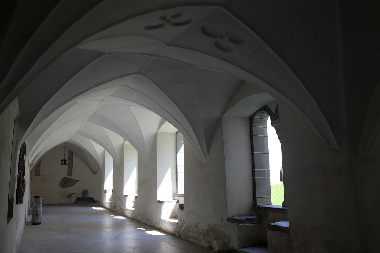 La luce del sole filtra dalle finestre ad arco di un chiostro in pietra.
